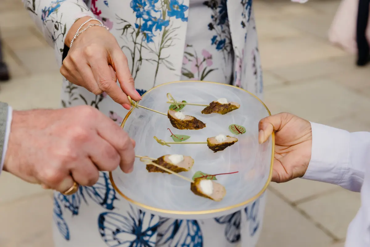 Guests picking canapés from a glass plate held by a waiter at Caswell House