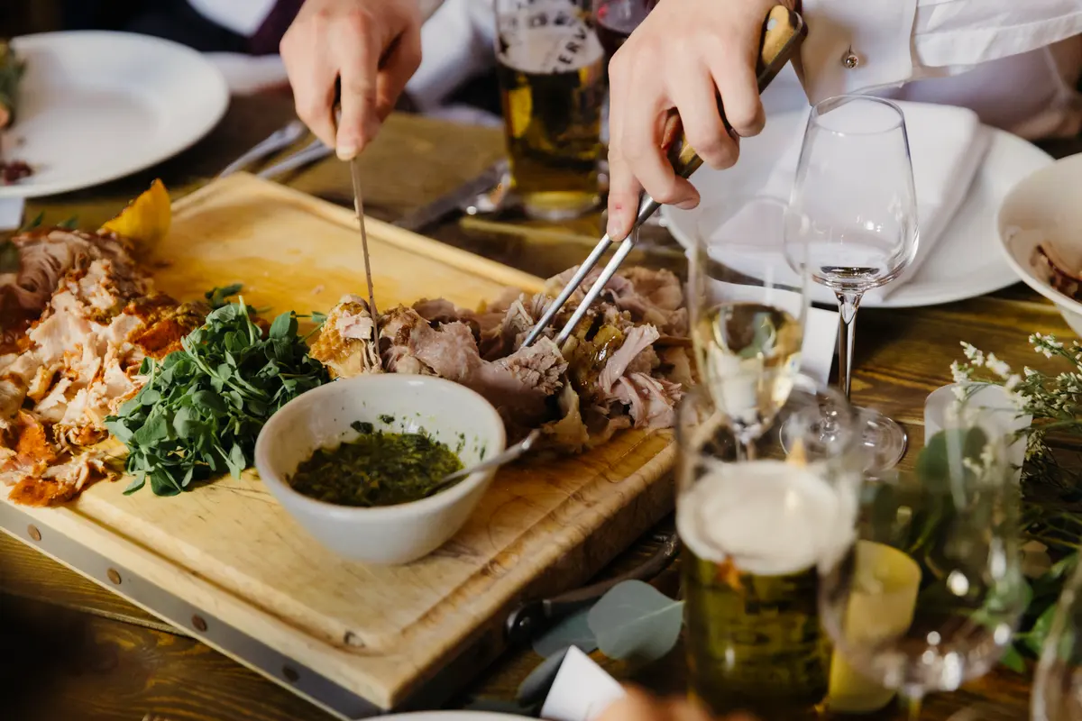 Carving slow-roasted meat on a wooden board with salsa verde at the wedding breakfast