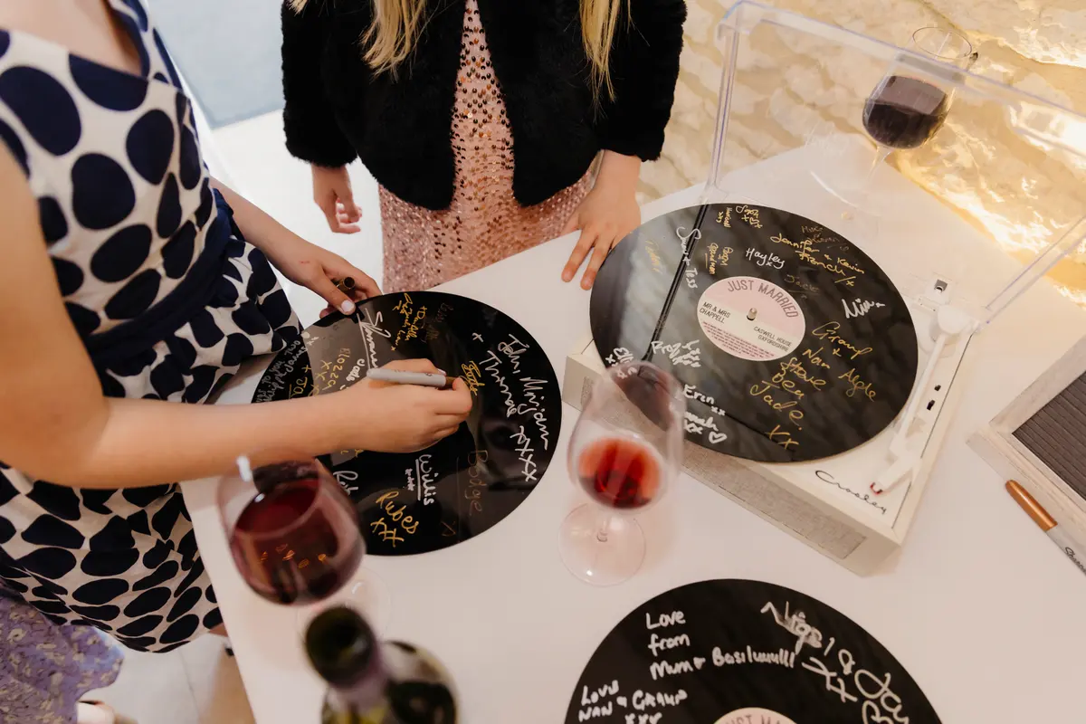 Guests signing vinyl records as a guest book beside a record player at Caswell House