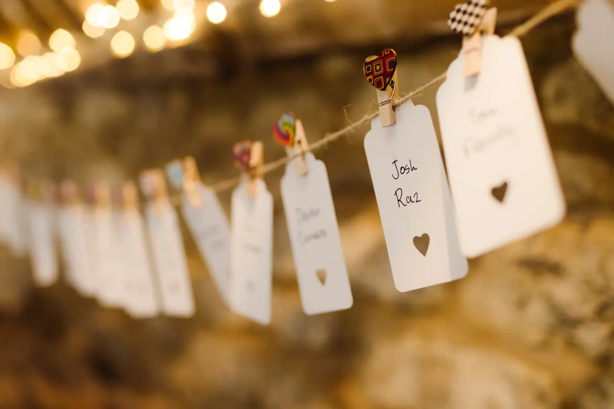 Handwritten name tags pegged to a string under fairy lights against a stone wall at Caswell House
