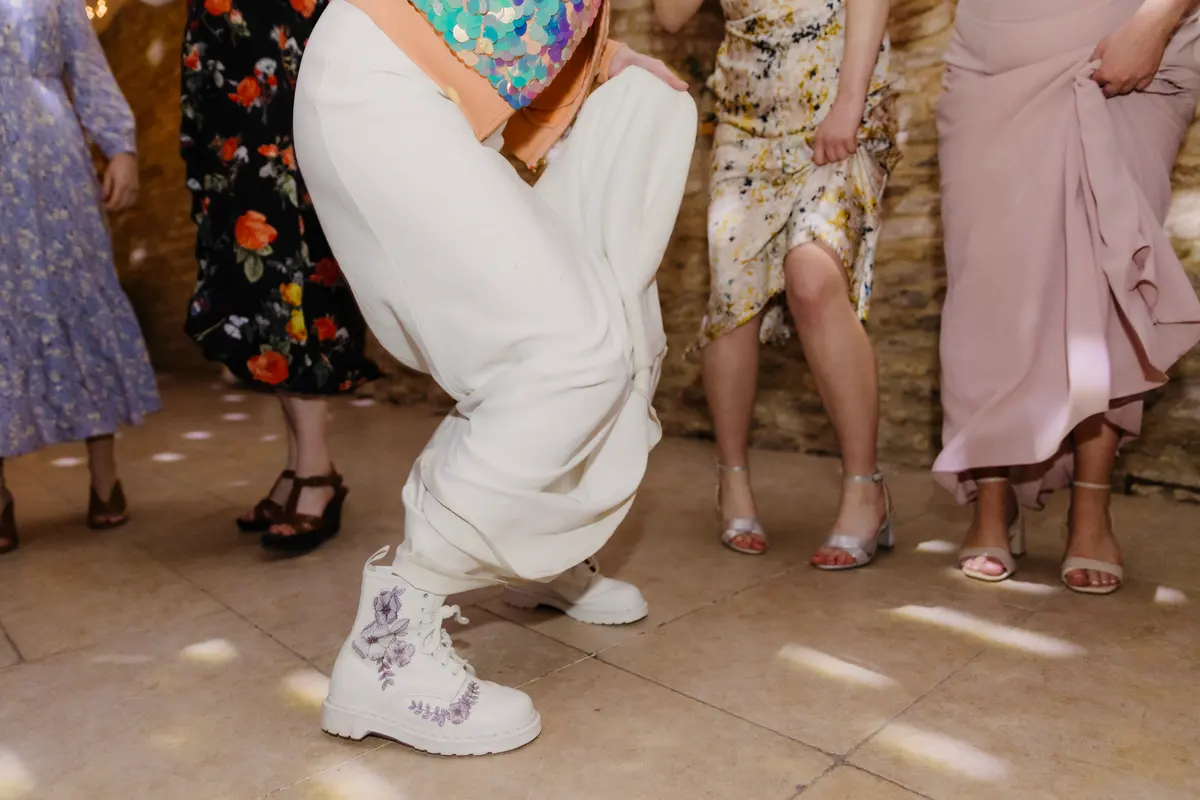 Guest in white trousers and embroidered boots doing a low dance move on the dance floor at Caswell House
