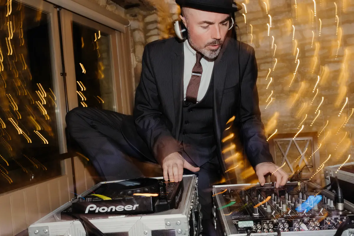 DJ in a hat and headphones leaning over his decks at an evening reception