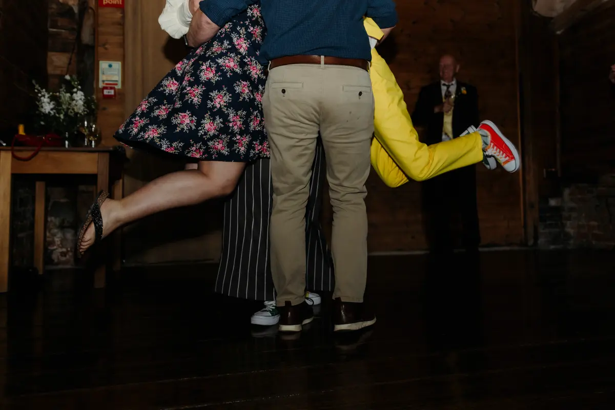 Guests mid-dance on the dark wooden floor, one kicking up a red trainer, at Lains Barn
