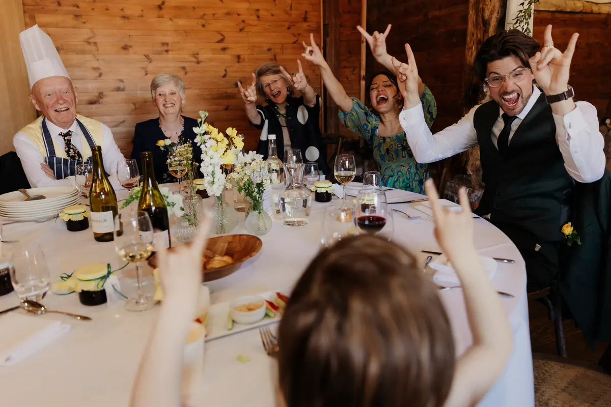 Guests at a round table making rock and roll hand signs, one in a chef's hat, at Lains Barn
