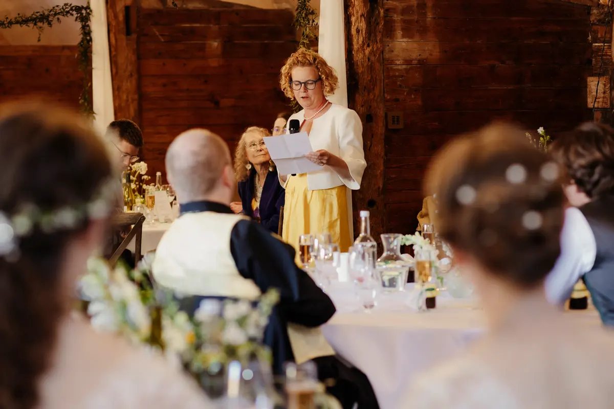 Woman in a yellow skirt reading her speech from notes at the top table at Lains Barn