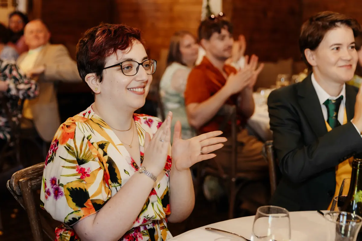Smiling guest in a floral dress applauding during the speeches at Lains Barn