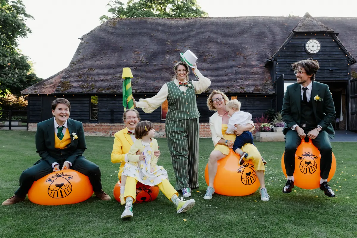 Wedding party in green and yellow outfits sitting on orange space hoppers outside Lains Barn