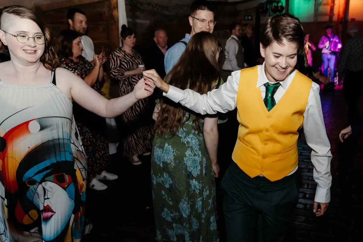 Guests holding hands and dancing in a line across the dance floor at Lains Barn