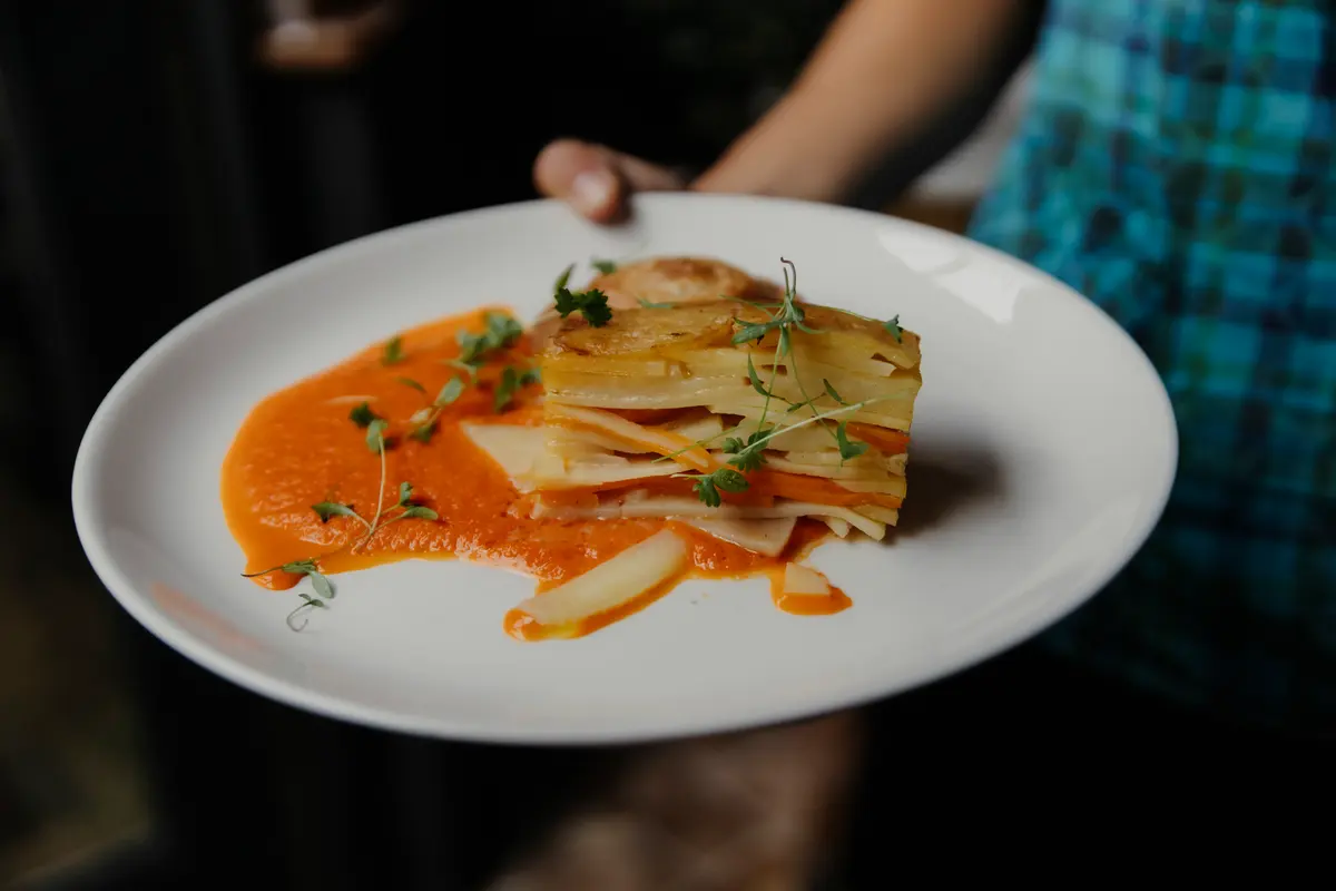 Plate of layered potato gratin with red pepper sauce and micro herbs