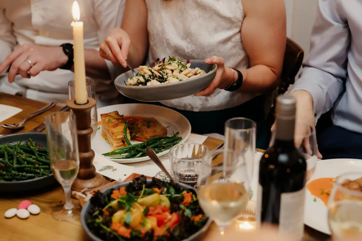 Guest serving a bowl of salad at a candlelit table with green beans and wine