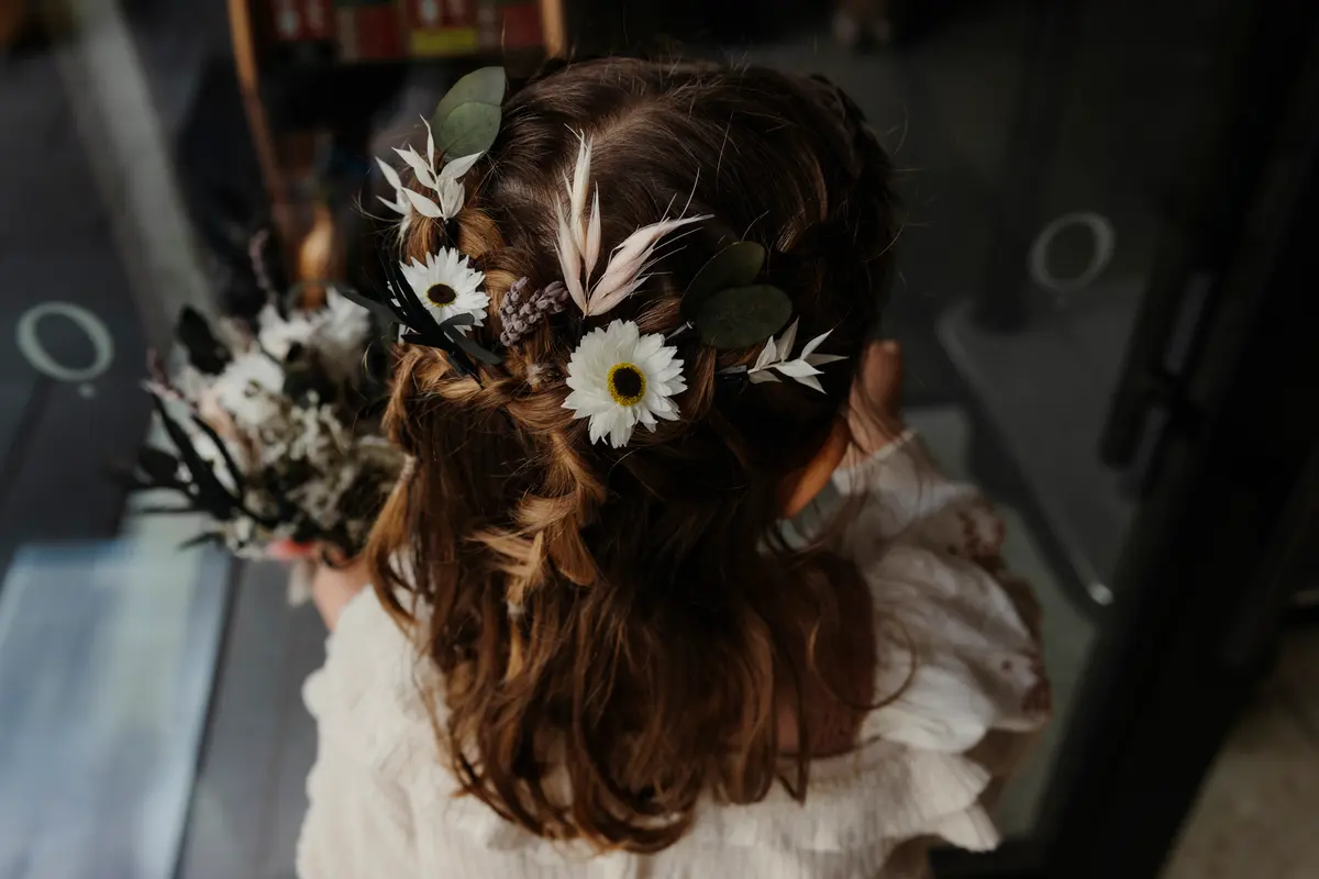 Flower girl's loose braided hair decorated with daisies, feathers and greenery