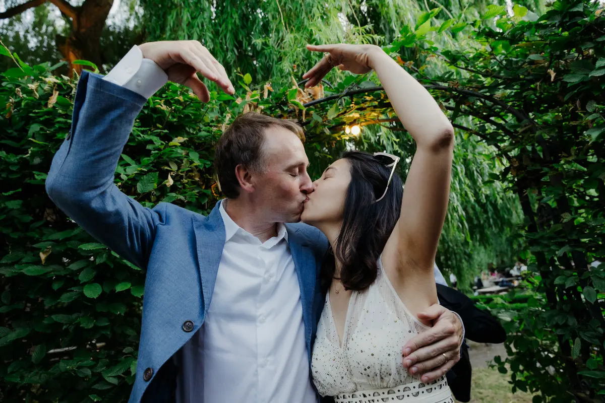 Couple kissing under willow trees while making a heart shape with their arms above their heads