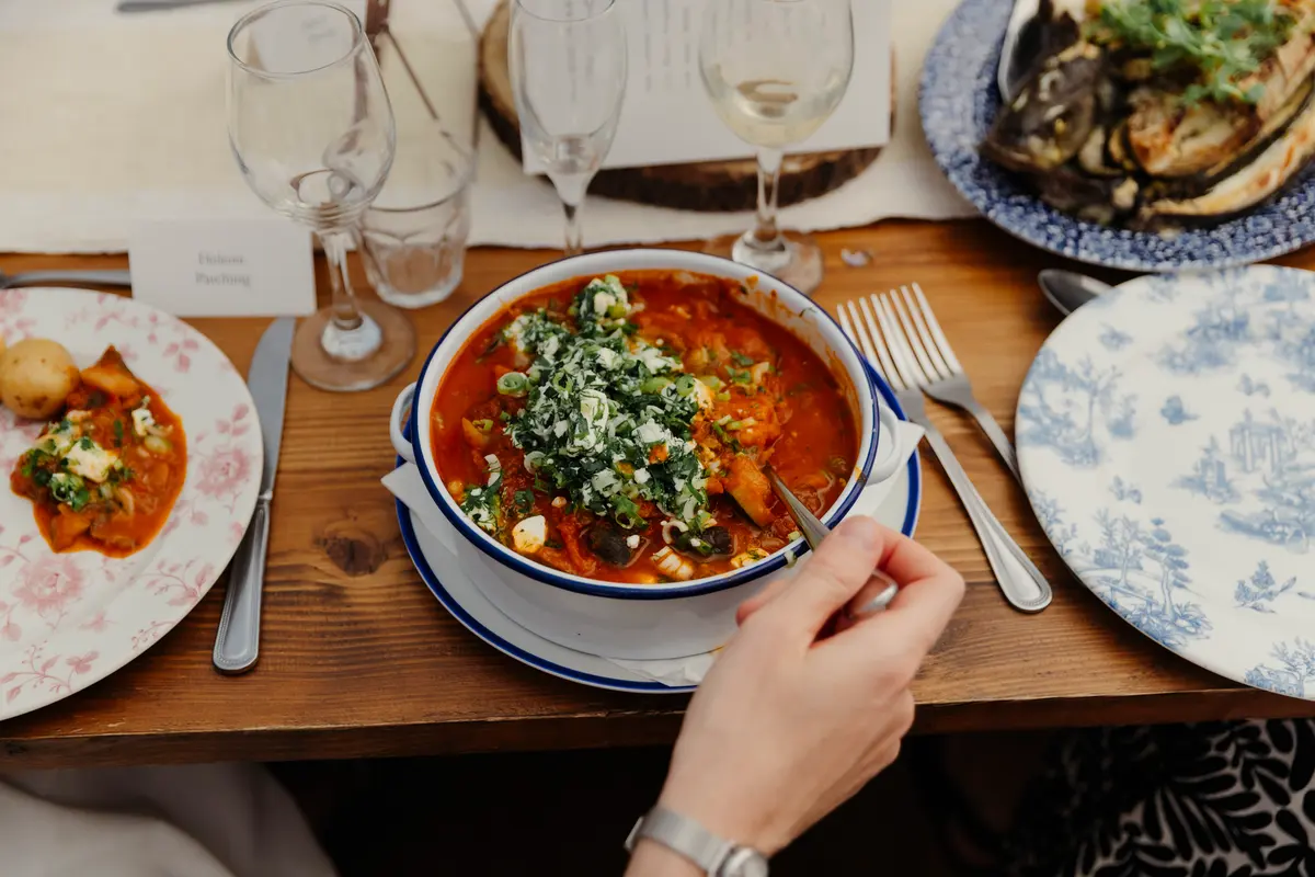 Guest eating a bowl of seafood stew at a wedding table laid with blue and pink patterned plates
